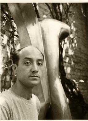Sepia toned image of Isamu Noguchi in front of one of his iconic sculptures